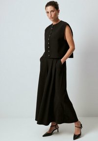Svart ärmlös topp med knappar, kombinerad med en lång svart kjol. Outfiten har en lös passform och en mjuk tygtextur.