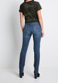 Jeans i denimblått med smal passform, med medelhög midja och fem fickor, i kombination med en figurnära kortärmad t-shirt i svart camouflage.