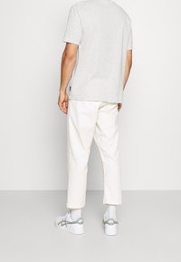 Grijze korte mouwen t-shirt met een relaxte pasvorm, gecombineerd met witte cropped broeken en witte sneakers met groene accenten.