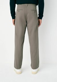 Men's straight-leg trousers, light gray color, cotton blend fabric, two back pockets with button closures, worn with white sneakers.
