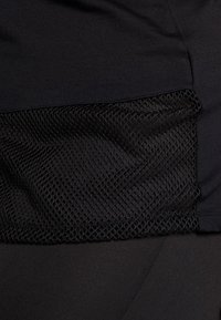 Zwarte sporttop met een gladde bovenlaag en een gestructureerd mesh onderpaneel, naadloos geïntegreerd voor ventilatie en stijl.
