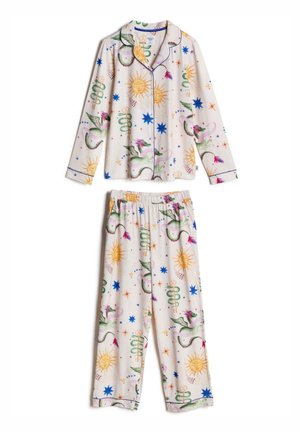 Femme portant une chemise blanche boutonnée avec des motifs colorés de soleil, d'étoile et de dragon, avec un liseré bleu sur le col et le devant.