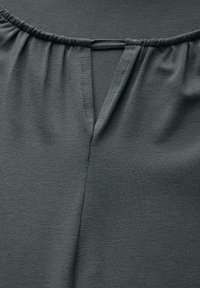 Ciemnoszary materiał o subtelnej teksturze, z marszczonym dekoltem i małym wycięciem w kształcie V z tyłu. Widoczne są detale szwów.