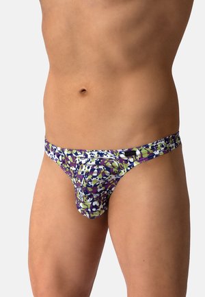 Männlicher Torso mit niedrig geschnittenen Slips mit einem farbenfrohen abstrakten Muster in Lila, Grün und Weiß auf hellem grauem Hintergrund.
