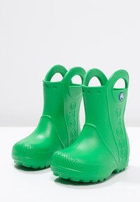 Botas de goma verdes con textura lisa, punta redonda y asas traseras para facilitar su uso. Presentan pequeños puntos en la suela y el logo de la marca.