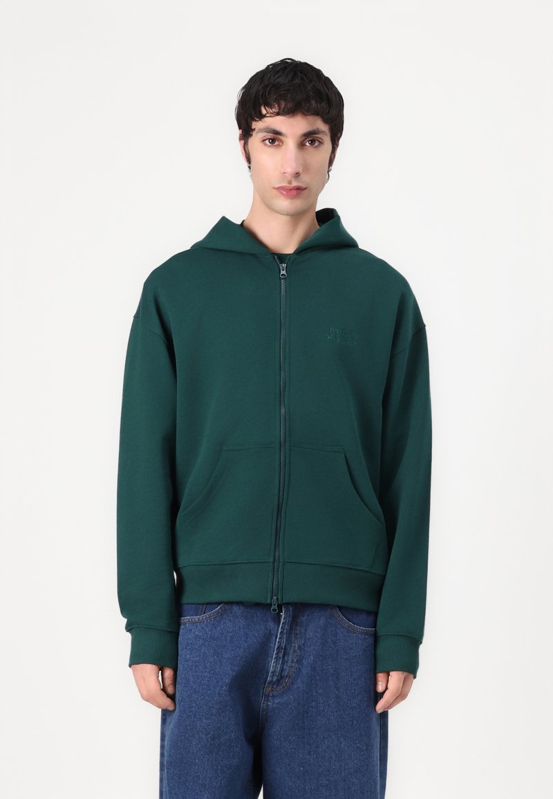 Grønn zip-up hettegenser laget av mykt stoff, med kengurulomme, ribbede mansjetter og hette. Pr präget logo detalj på brystet.
