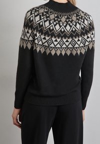 Svart tröja med ett geometriskt stickat mönster i vitt och grått, med hög hals och ribbad nederkant. Mjuk textur.