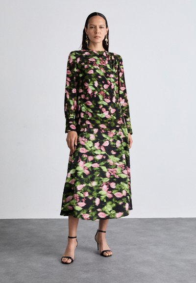 Langarmige bloemenjurk met een zwarte basis en roze en groene patronen; vloeiende silhouette; gecombineerd met zwarte enkelbandhakken.