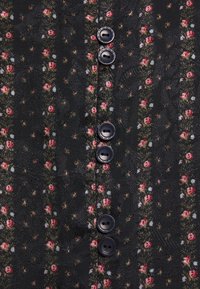 Blusa in tessuto nero con motivo floreale, caratterizzata da piccoli fiori rossi e accenti verdi; sei bottoni neri lungo il centro anteriore.