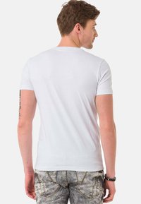 Weißes Baumwoll-T-Shirt mit kurzen Ärmeln, figurbetontem Design und glatter Textur, von hinten betrachtet. Akzente sind die Nähte am Saum.