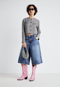 Veste cropped en tartan gris avec des boutons, large culotte en denim bleu, bottes de cowboy roses et un petit sac à main en pied de poule.