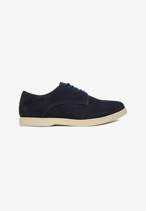 Navyblauer Wildleder-Herrenschnürschuh mit beiger Gummisohle, niedrigem Absatz und abgerundeter Spitze, von rechts auf weißem Hintergrund gezeigt.