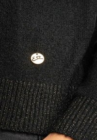 Pullover nero con lavorazione a maglia testurizzata e orlo a coste. Include un piccolo etichetta rotonda dorata con un logo minimalista.