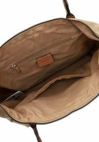 Interno di una borsa in tessuto beige con una tasca con zip e un'etichetta in pelle marrone, caratterizzato da una superficie liscia e dettagli di cucitura a contrasto.