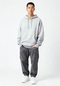 Felpa con cappuccio grigio chiaro con tasca frontale, abbinata a pantaloni cargo grigio scuro dalla vestibilità ampia, con tasche laterali e polsini elastici, indossata con sneaker bianche.