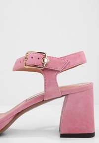 Sandale à talons hauts en daim rose avec un large talon bloc et une bride de cheville réglable dotée d'une boucle dorée.