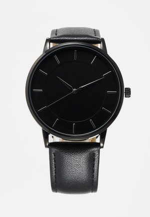 Zwarte polshorloge met eenvoudige zilveren uurmarkeringen, drie dunne wijzers en een getextureerde zwarte leren band.