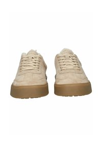 Zapatillas de ante beige con una superficie texturizada, puntera redonda y suela de goma marrón claro. Presentan cordones planos y un logotipo sutil en la lengüeta.