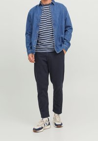 Denim button-up shirt, striped navy and white T-shirt, dark pants, and sneakers with beige and navy accents. Casual outfit.