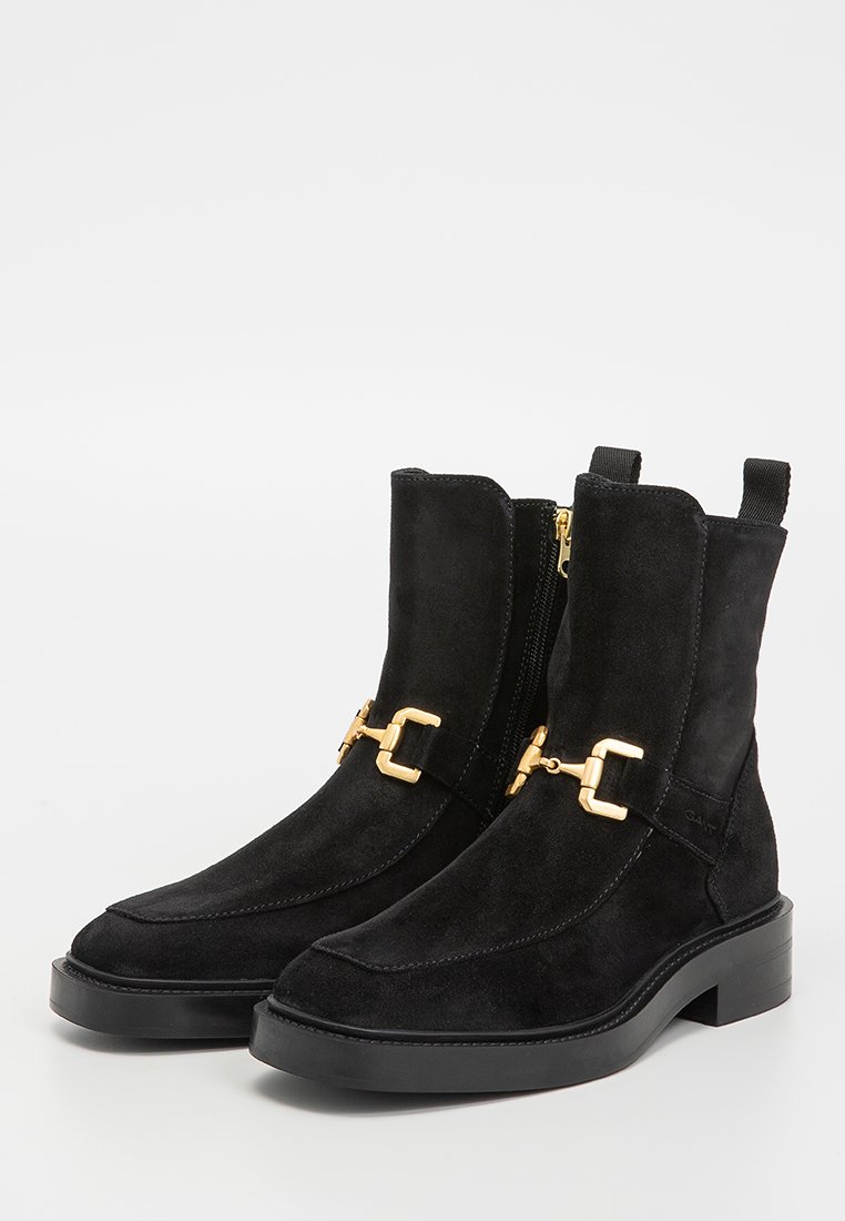 Botas de tobillo de ante negro con puntera redondeada, acentos de hardware dorado, cremalleras laterales y suela de goma gruesa. Textura suave en todo.