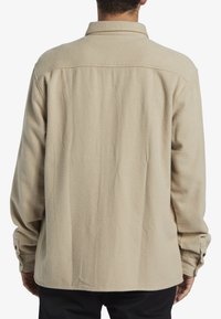 Beige fleece shirt with a relaxed fit, featuring a classic collar and buttoned cuffs, displaying a soft texture and subtle seam details.