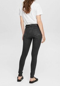 Jeans skinnies negros de cintura alta, con una textura de mezclilla suave, cinco bolsillos y un diseño clásico de trabillas para cinturón. Combinados con una camiseta blanca y sandalias.