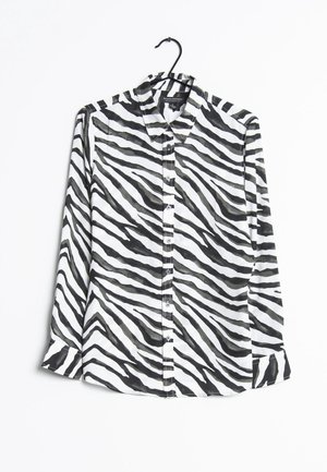 Zwart-wit zebraprint overhemd met lange mouwen en knopen, hangend aan een zwarte hanger tegen een witte achtergrond.