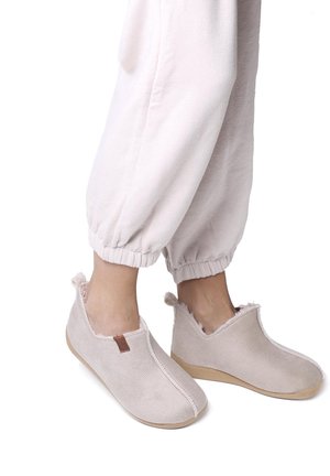 Lichtbeige instappers van textiel met een zachte, pluizige voering en ruwe randen. Voorzien van een bruine leren accent.