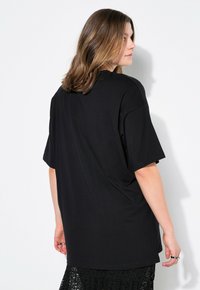 Camiseta negra de gran tamaño hecha de algodón, con mangas cortas, escote redondo y un corte relajado, con textura suave y sin patrones visibles.