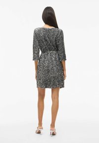 Robe noire et argent scintillante avec des manches trois-quarts, taille ceinturée et jupe évasée ; présente des sequins pour la texture et l'éclat.