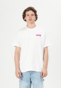 Hvit bomulls t-skjorte med et rosa "Originals" logo-patch på venstre bryst. Korte ermer, rund hals, avslappet passform. Lett teksturert stoff.