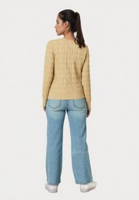 Pulover galben cu torsadă și tiv striat, asortat cu blugi albastru deschis, cu croială largă, și adidași albi, văzut din spate.