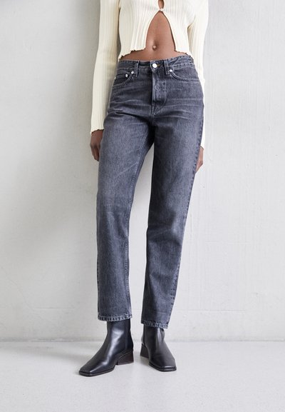 Jean noirs taille haute avec une coupe droite, texture légèrement délavée, associés à des bottines noires à bout carré. Design minimaliste.