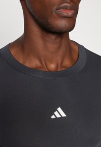 Sort atletisk t-shirt med rund halsudskæring, glat tekstur og et hvidt Adidas-logo med tre striber på venstre brystområde.