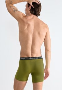 Boxer shorts verde oliva con elastico nero recante la scritta bianca "sloggi". Texture liscia, vestibilità aderente e design di lunghezza media fino alla coscia.