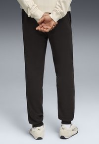 Sorte sweatpants med tapered ben og ribbede manchetter, matchet med beige træningssko med sorte accenter. Glat stoftekstur.