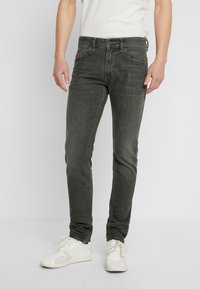 Herrjeans med smal passform i mörkgrön denim, med en klassisk design med fem fickor, dragkedja och subtila blekningar. Kombinerade med vita sneakers.