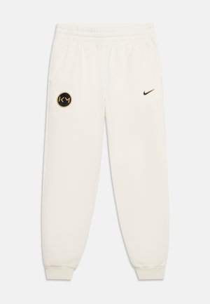 Pantalon de survêtement blanc Nike avec taille et poignets élastiques, arborant un logo KM noir et doré sur la cuisse gauche et un petit swoosh Nike noir sur la cuisse droite.