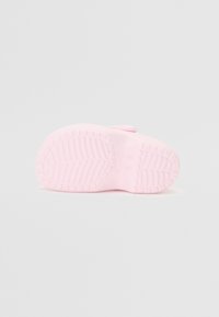 Vaaleanpunainen kumikenkien pohja, jossa on teksturoitu kulutuspinta, pyöreä muoto ja yksi hihnatieto varmistaakseen tukevan istuvuuden. Pintakäsittely on sileä koko matkalta.