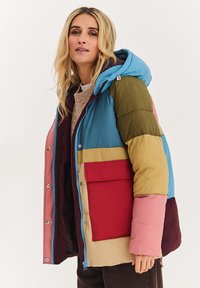 Barevná péřová bunda s kombinací modrých, zelených, červených a béžových panelů, s kapucí a přední kapsou na zapínání na cvočky.