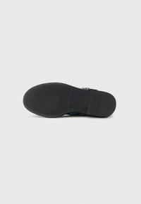 Potplat crne cipele s teksturiranim potplatom i malom petom na jednostavnoj svijetloj pozadini.