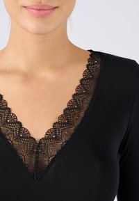 Top nero con scollatura a V profonda, dettagliato con delicata bordatura in pizzo nero, caratterizzato da una superficie liscia e un design aderente, che mette in risalto il décolleté.