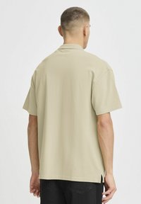 Lys beige kortermet skjorte med avslappet passform. Har klassisk krage, sideslisser og en jevn tekstur. Enkel design.