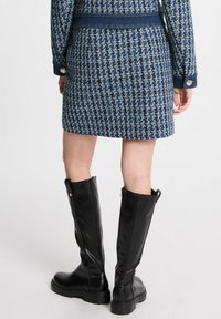 Falda de mezcla de lana en patrón de espiga azul marino con cinturilla de mezclilla; combinada con botas de cuero negras hasta la rodilla con cremalleras laterales.