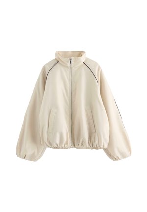 Beige jakke med lynlås, høj krave, elastisk kant og ærmegab, to forlommer samt sort piping langs skuldersømmene.