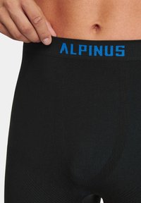 Czarne legginsy termiczne z prążkowaną teksturą i szerokim pasem w talii, na którym znajduje się niebieski napis "ALPINUS" z przodu.