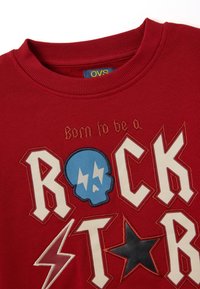 Sudadera roja con un atrevido texto "ROCK STAR" en multicolor y un gráfico de calavera azul con acentos de rayos, todo sobre una tela texturizada.