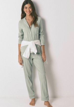 Lysegrønt ribbet pyjamasæt lavet af blødt stof, med en skjorte med knapper og lomme samt matchende bukser, bundet med et hvidt bælte.