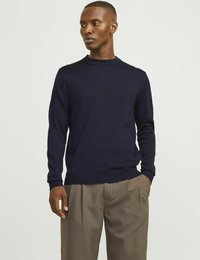Marineblauw gebreid sweater met lange mouwen, ronde halslijn en ribgebreide manchetten. Gecombineerd met lichtbruine wijde broek. Soepele structuur.