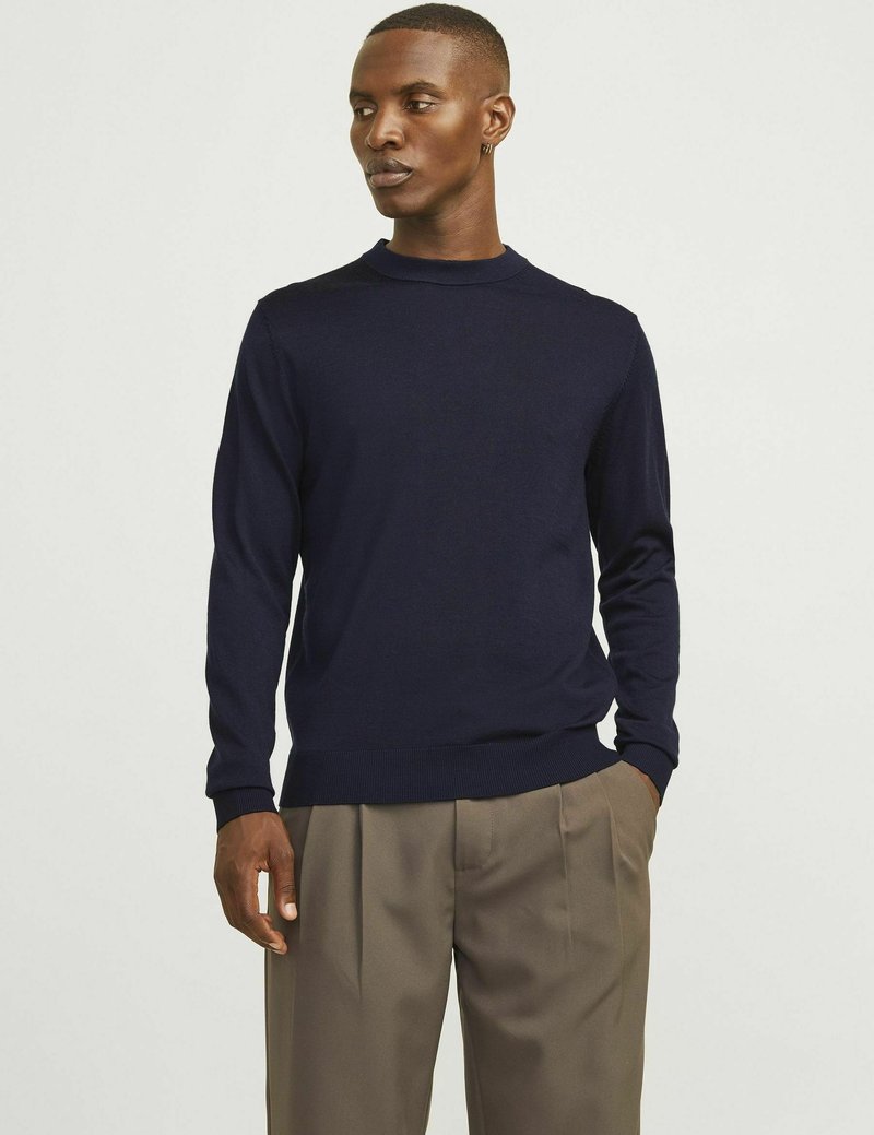 Marineblauw gebreid sweater met lange mouwen, ronde halslijn en ribgebreide manchetten. Gecombineerd met lichtbruine wijde broek. Soepele structuur.